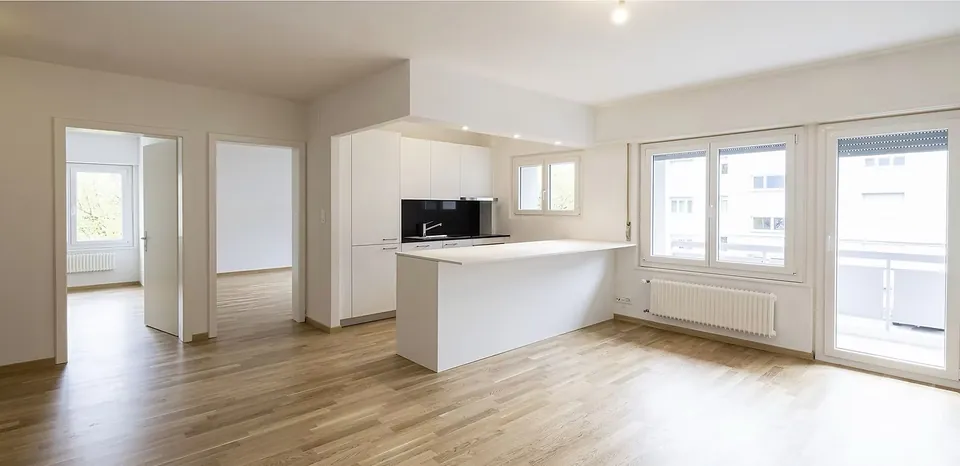 Séjour de l'appartement Beaulieu après rénovation complète : cuisine blanche ouverte sur le séjour, parquet chêne et murs repris